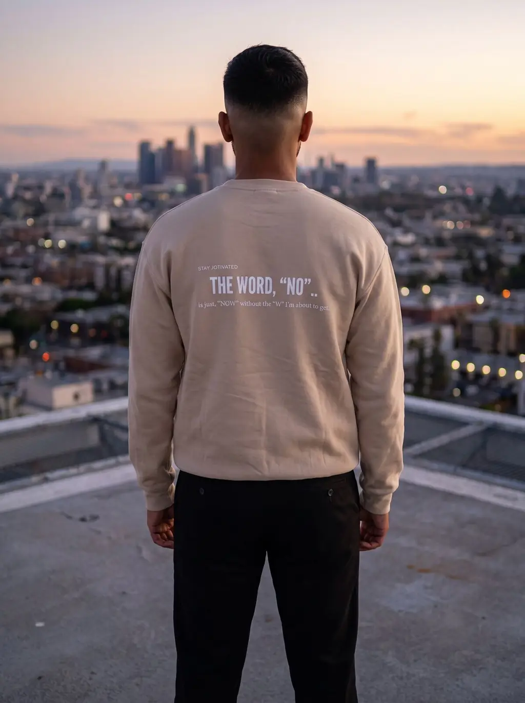 Man on a rooftop at dusk wearing the tan crewneck, back print visible